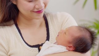 美丽迷人的亚洲妈妈抱着她刚出生的宝宝，亲吻着宝宝的鼻子，甜甜的，可爱的。快乐的妈妈和宝宝一起看着宝宝，带着爱微笑。母亲和婴儿新生儿概念视频素材模板下载