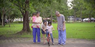 妈妈一边陪爷爷奶奶走路，一边帮女儿学骑自行车