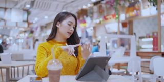 年轻聪明休闲亚洲女性企业家企业所有者或自由职业者使用智能手机平板电脑在美食广场公共区域工作，年轻的亚洲自由职业者使用平板设备在线管理业务