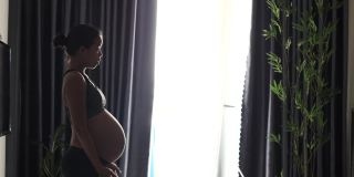 一个怀孕的亚洲妇女在家里做热身和伸展运动。