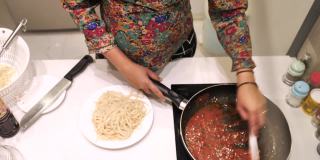 一名孕妇正在厨房里用红酱准备意大利面。