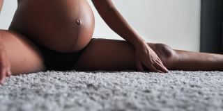 一个大肚子的女人坐在家里的地毯上做伸展运动。