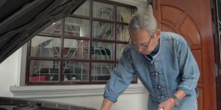 亚洲老爷爷在离家前戴着眼镜检查他的旧车的机油水平。退休的生活。