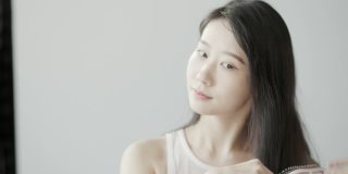 一位年轻漂亮的韩国女子有着长长的黑发。她对着镜子梳头，住在一个白色的房间里