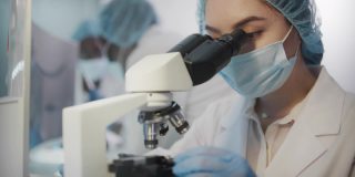 多元化的团队在现代化的实验室中工作。亚洲科学家使用显微镜。穿着防护工作服