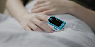 一个女人躺在床上，食指上拿着脉搏血氧计。手的特写镜头。真正的时间。血液中氧含量测定的概念