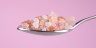 喜马拉雅粗糙的岩盐在一个粉红色的背景上的勺子。落橙粗晶