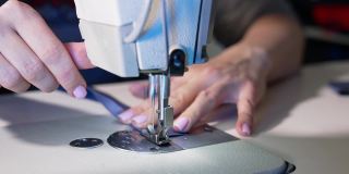 女性的手在缝制衣服。在服装设计车间使用缝纫机进行裁缝工作