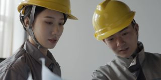 两个身穿工作服、头戴钢盔的年轻工程师正在观看设计图纸，讨论施工方案、设计师和建筑师