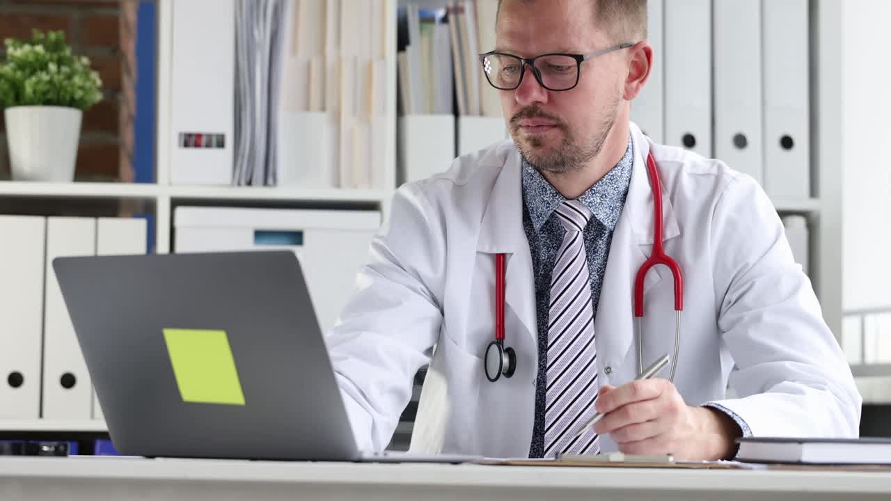 年轻的医生戴着眼镜看着笔记本电脑屏幕，在4k电影里写医疗文件