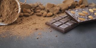 用杏仁做巧克力棒，甜点，手工糖果。由牛奶和黑巧克力块组成，可可粉在黑色背景上。桌上的糖果工艺品