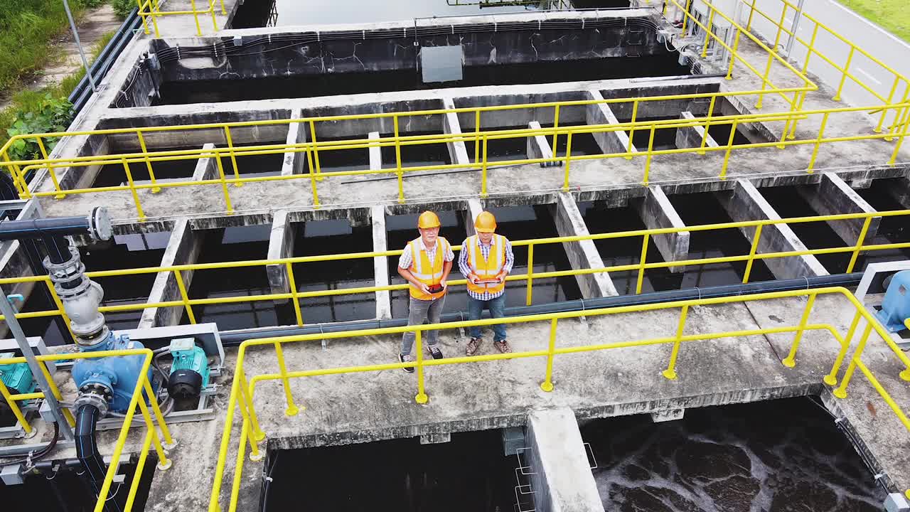 亚洲男工程师穿着反光背心和头盔检查工业工厂的废水处理池。
