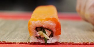寿司厨师将一卷米饭和鳟鱼裹在垫子上。亚洲美食，寿司餐厅。煮滚。4 k。