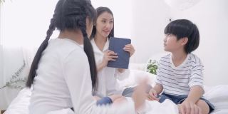 亚洲的儿子和女儿从他们的兄弟手中抢夺平板电脑，年轻的母亲对一个试图停止争吵的孩子的恶作剧感到压力
