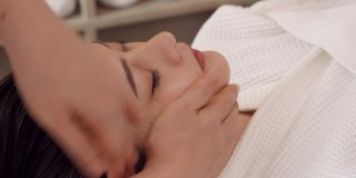 亚洲妇女在美容沙龙健康水疗按摩按摩的按摩师正在给女人面部按摩躺在床上