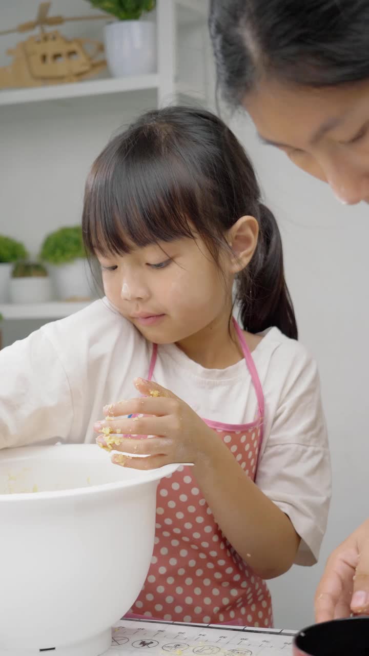 快乐的亚洲孩子在家里学习做饼干，女孩在搅拌碗里打面团。