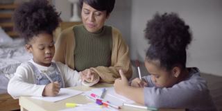 亚洲母亲帮助她的两个非洲女儿和教绘画作业在公寓
