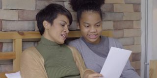 非洲裔美国女孩展示她的家庭作业或贺卡给年轻的亚洲妇女惊喜后完成了母亲节的研究