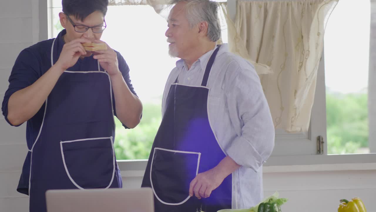 快乐的亚洲年轻人和老父亲在家里的厨房里一起准备美味健康的沙拉，享受周末