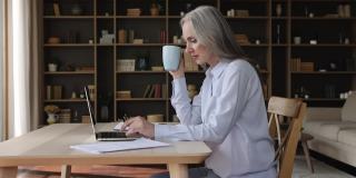 成熟的女人喝茶，用笔记本电脑坐在桌边