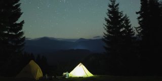 在星星闪烁的夜空下，在漆黑的群山中，露营地的游客帐篷旁，点着篝火休息。积极的生活方式和户外生活理念