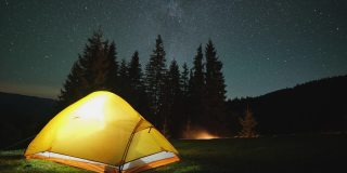 夜晚的星空下，明亮的帐篷在黑暗的山上闪闪发光。积极的生活方式和徒步旅行的理念