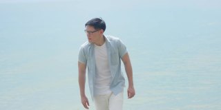 一名戴着眼镜的英俊青年带着一种孤独和失望的表情走在海滩上