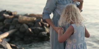 快乐的金发妈妈和可爱的女儿一起在日出的海滩上散步