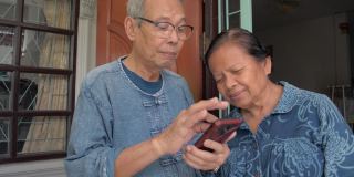 一位亚洲老人，灰白头发，在家里用智能手机上的应用程序教他的妻子。高级一些的生活方式。退休生活与数码设备。