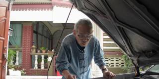 亚洲白发老人戴着眼镜，在家里清洗和检查他的旧车的发动机状况。老年人退休生活。