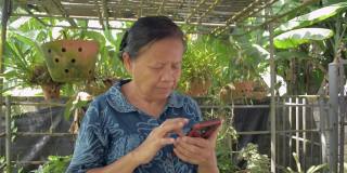 身着休闲装的亚洲老奶奶在花园里用智能手机上的应用程序与孙女视频通话。
