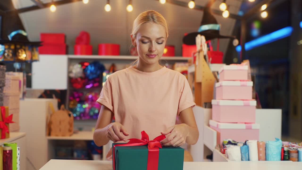 前视图的年轻女子设计师包装圣诞礼品盒系红丝带和装饰美丽的蝴蝶结站在桌子的假日商店。