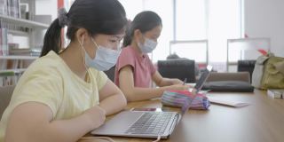 新常态亚洲女孩在图书馆网上学习戴口罩防止冠状病毒covid - 19的概念技术教育