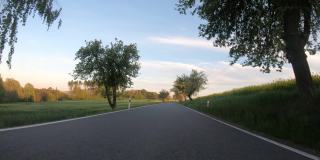 汽车在傍晚行驶在春乡的乡间小路上。有树的景观，有阳光的蓝天，旅游和交通的概念。观点观点