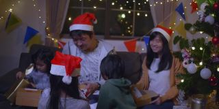 快乐的一家人带着女儿戴着圣诞帽，在圣诞节的时候聚在一起，享受打开礼品盒的乐趣