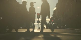 日落时人们穿过街道的慢镜头剪影。城市和城市生活理念