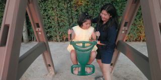 4K慢镜头:亚洲妈妈和可爱的女儿在公共游乐场开心地玩秋千。