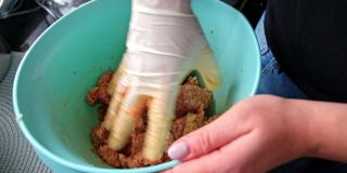 白种人妇女在厨房准备牛排鞑靼与她的手揉压和混合生的未煮碎的肉，戴着乳胶保护手套，以避免沙门氏菌