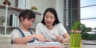 亚洲妈妈在家庭学校和网络课堂上帮助她的女儿做涂色书作业