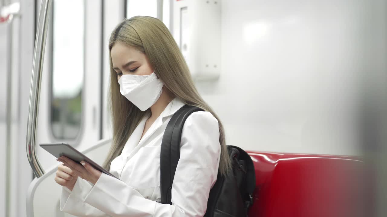 戴着防护口罩的年轻女子在地铁上使用电子平板电脑