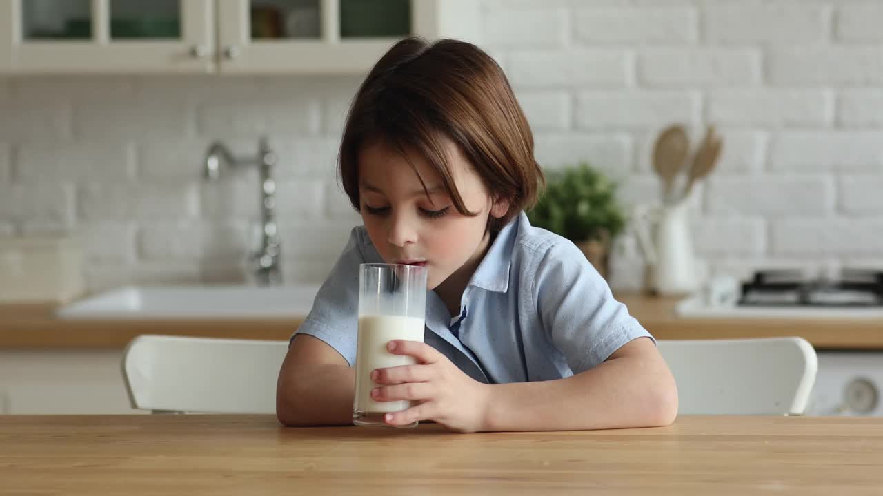 可爱的口渴的小男孩喝着一杯牛奶。