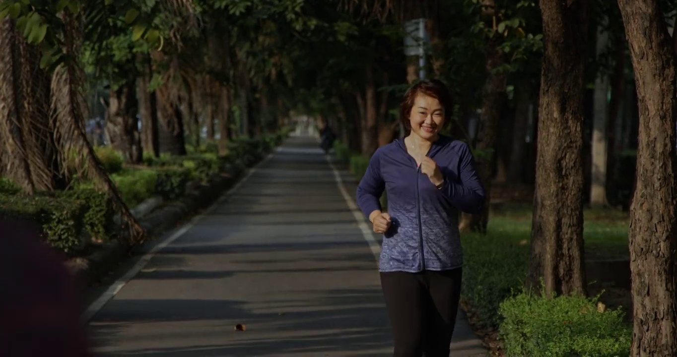 夏天的早晨，一群亚洲人在公园里愉快地慢跑。男人和女人每天跑步有健康的身体。城市人的假期周末活动和锻炼。概念的锻炼