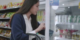 一位妇女在冰箱里选择饮用水，一位亚洲女商人穿着蓝色的休闲装正在购买商品和服务