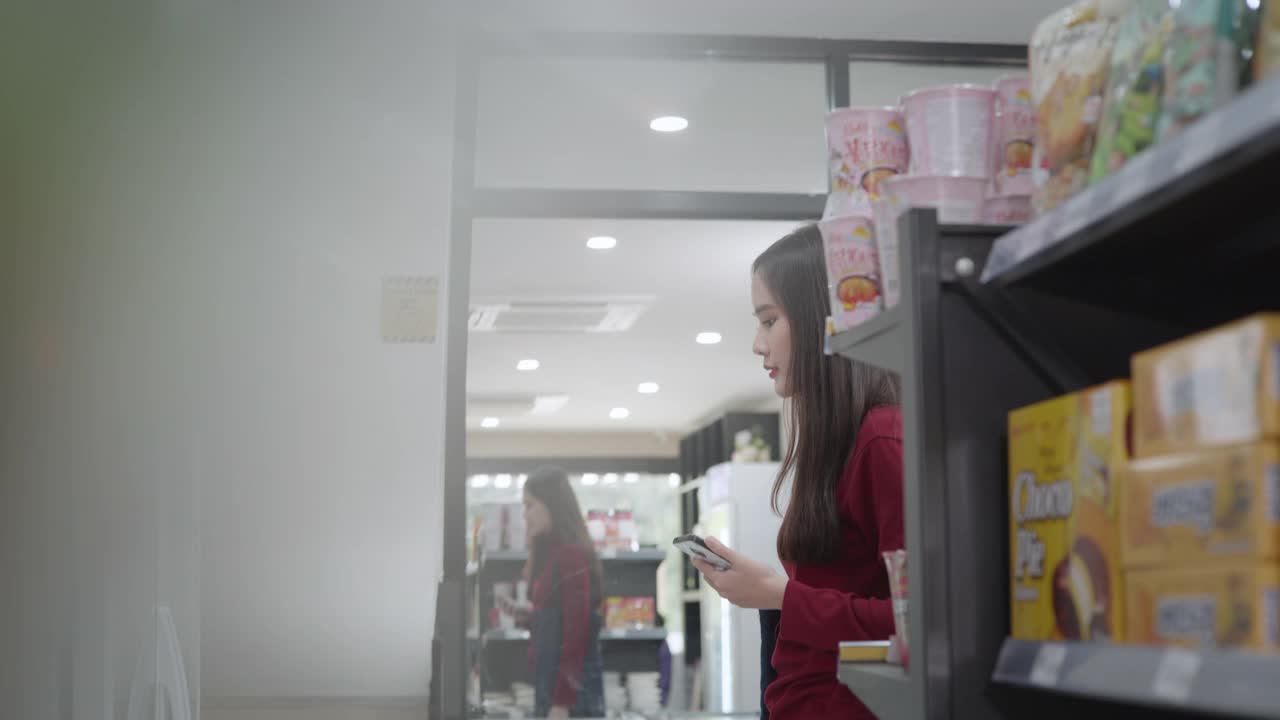 一名亚洲女商人身穿红色便装，正在一家杂货店购买商品和服务