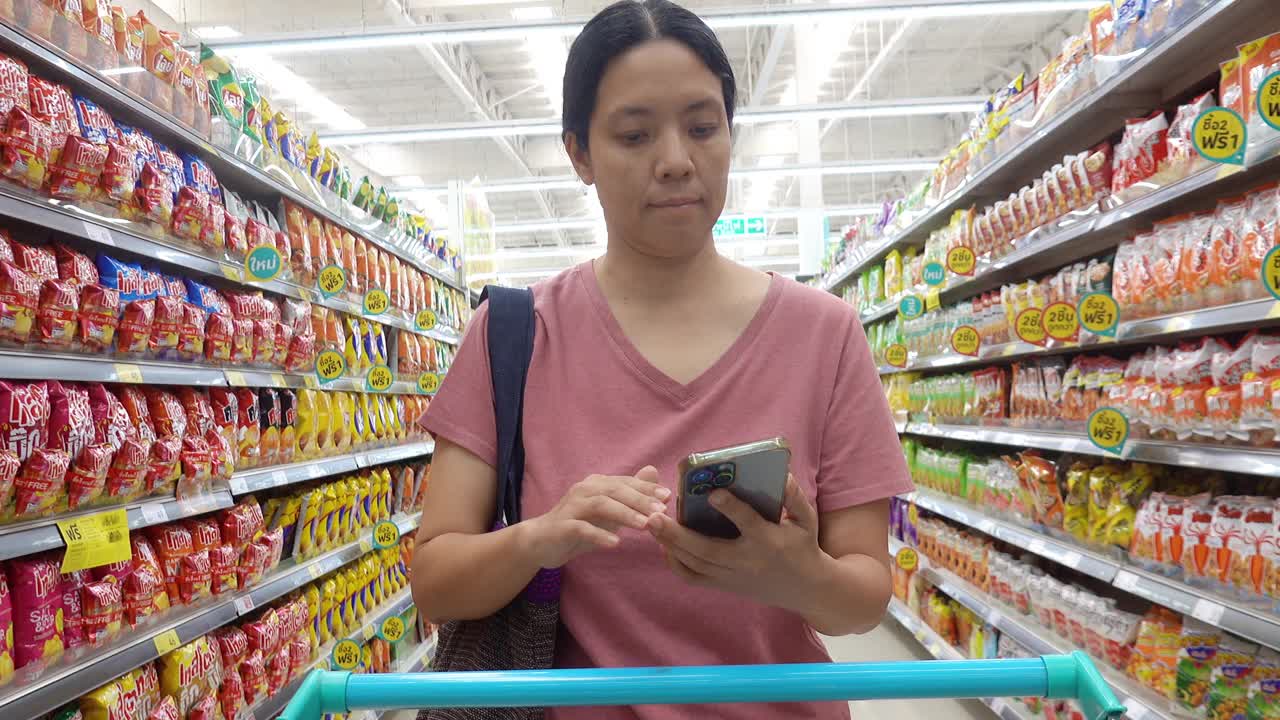 亚洲成熟女性带着智能手机和可重复使用的购物袋在杂货店购物