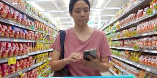 亚洲成熟女性带着智能手机和可重复使用的购物袋在杂货店购物