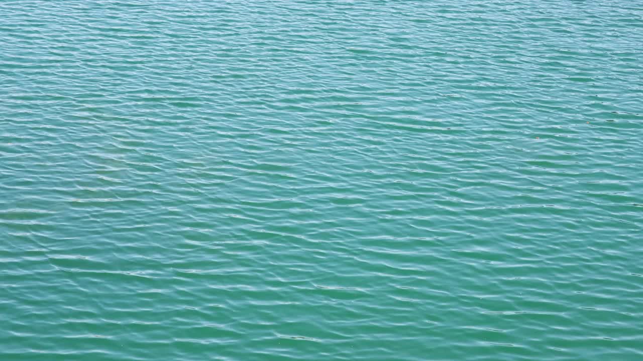 无缝无人机在碧绿的湖水涟漪接近视图。鸟瞰图的海或海洋与美丽的波浪图案的景观，无尽的海蓝宝石水在夏天的日子