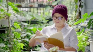 亚洲老年癌症阅读书籍，在花园放松，健康理念，健康保险，人寿保险视频素材模板下载