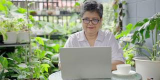 一位上了年纪的亚洲妇女懒洋洋地躺在她家后院的笔记本电脑上，过着快乐的退休生活。健康养生理念，老年科技