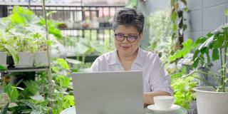 一位上了年纪的亚洲妇女懒洋洋地躺在她家后院的笔记本电脑上，过着快乐的退休生活。健康养生理念，老年科技